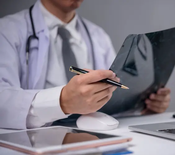 Doctor with stethoscope reviewing medical records and writing notes on clipboard at desk in office